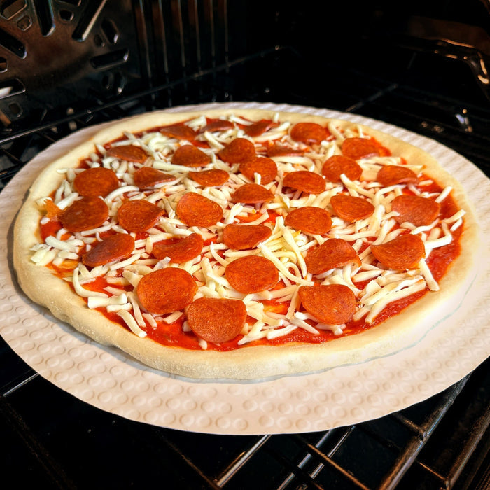 Uncooked pizza with pepperoni and cheese on a baking tray inside an oven.