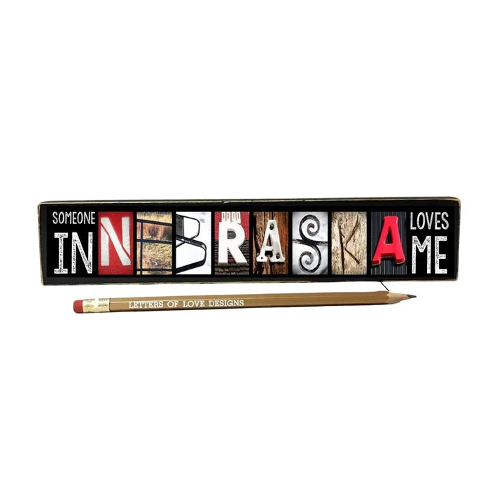Decorative sign with 'Someone in Nebraska loves me' text and a pencil on a white background
