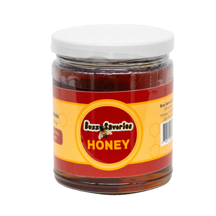A glass jar filled with honey, labeled Buzz Savories HONEY, with a white lid on a plain background.