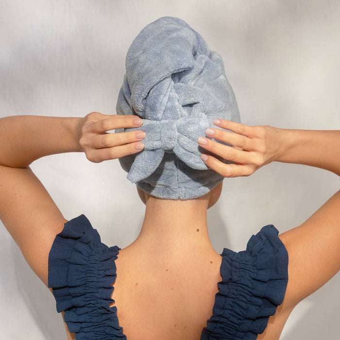 Woman wearing blue plush microfiber hair towel turban with bow, hands adjusting towel