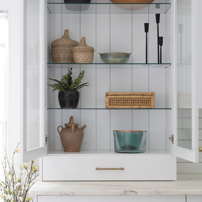 White kitchen cabinet with glass doors open to shelves decorated with wood bowls and kitchen accessories