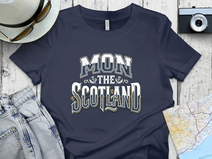 Dark blue t-shirt with "MON THE SCOTLAND" text, flat lay with jeans and camera.