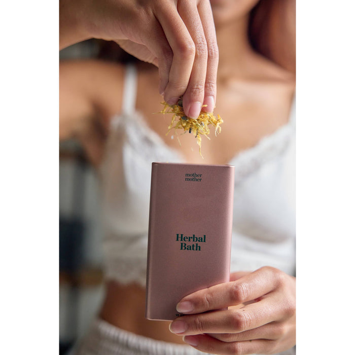 Woman holding MOTHER MOTHER Organic Herbal Sitz Bath box with dried herbs above it