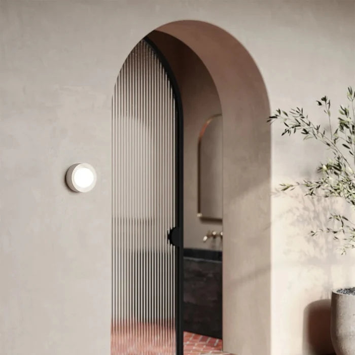 Archway leading to a bathroom with a black door and light fixture on the wall.
