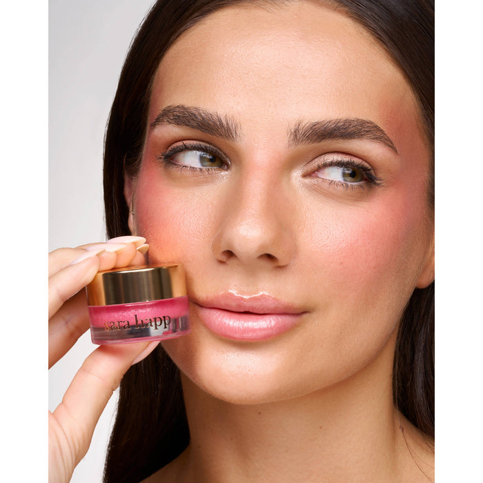 Woman holding Sara Happ Raspberry Sorbet Kiss Kit lip product near face, demonstrating application