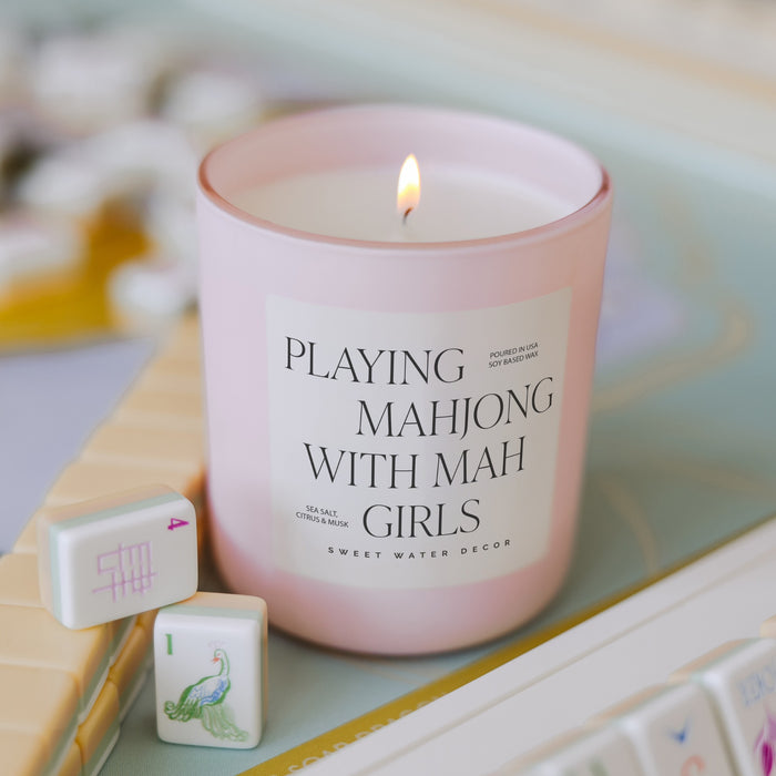 Pink soy candle with mahjong tiles on wooden surface with flowers