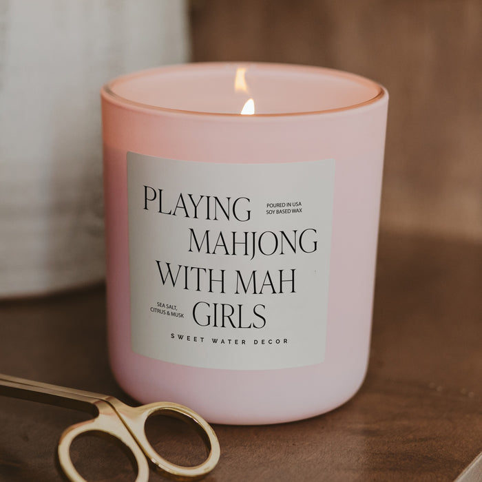 Pink soy candle with mahjong-themed label on wooden surface with decorative scissors