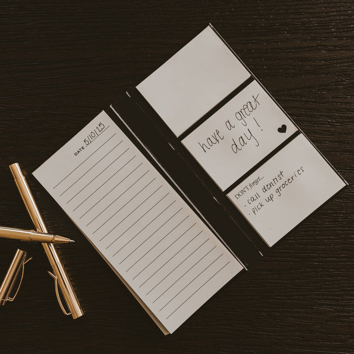 Portable sticky notes booklet displayed on dark wood with gold pen and clips, showing lined pages and 'have a great day' cover