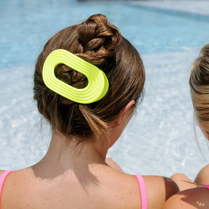 Neon yellow hair clip worn in beach setting with ocean waves in background