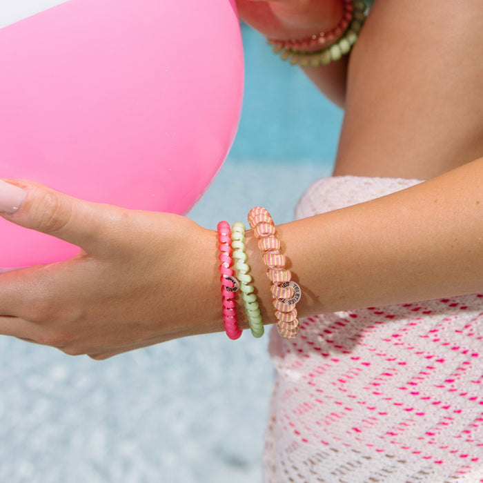 Woman wearing colorful beaded hair ties on wrist holding pink balloon at beach